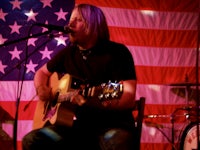 a man playing an acoustic guitar in front of an american flag