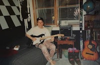 a man sitting on a bed with a guitar in his room