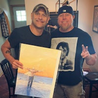 two men holding up a painting of a man in a hat
