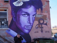 a man is standing in front of a building with a mural of prince