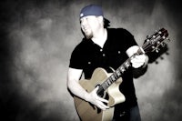a man holding an acoustic guitar in front of a dark background