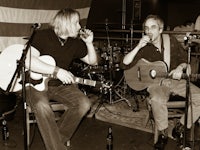two men playing guitars in front of an american flag
