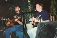 two men playing acoustic guitars in front of a microphone