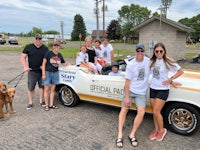 a group of people posing in front of a car with a dog